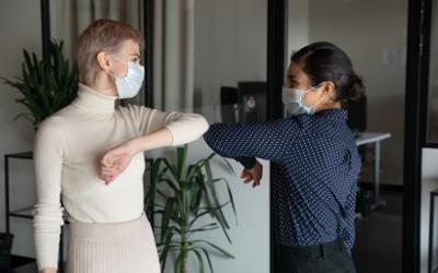 Two women wearing face masks and bumping elbows