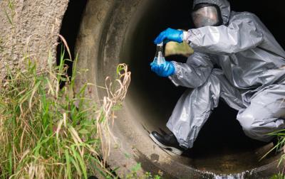A man in a protective suit and mask in a large sewer took a sample of water for analysis