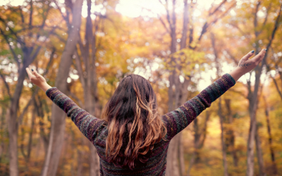Woman with arms outstretched standing amongst trees