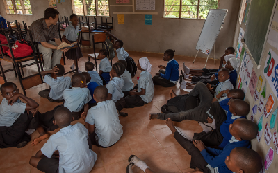 African school children sitting on the floor listening to teacher reading a book