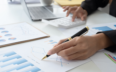 Person's hands with a pen in one hand, and a calculator and graph papers on a table