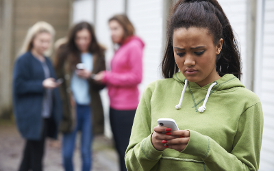 Girl wearing a green sweatshirt, looking at her phone, with a group of girls in the background