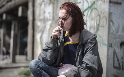 Teenage girl, smoking a cigarette, sitting in front of a graffiti-covered wall