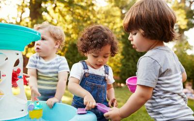 Three young children playing with a water table in the garden