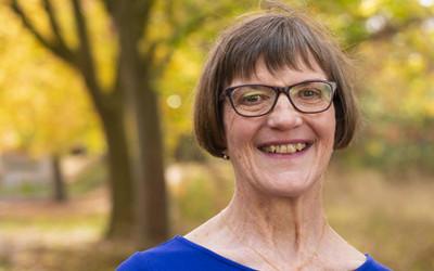 Lady wearing glasses and a blue top, standing in front of trees