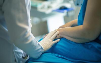 A woman wearing a blue dress with her hands in her lap and a doctor wearing a white coat and white gloves