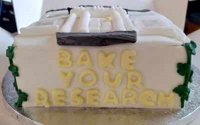 White, squrare cake with the words 'Bake Your Research' iced onto the side