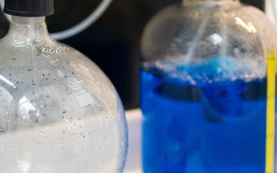 Two glass bottles of water, one with clear water in and one with blue water in