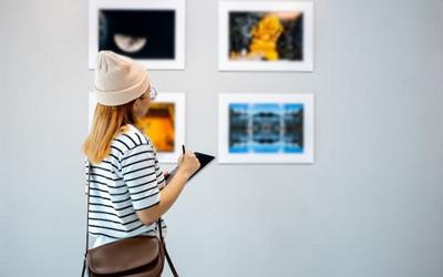 Woman wearing a hat and a striped t-shirt, looking at paintings on a wall